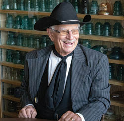 A man wearing a cowboy hat and glasses is sitting at a table with a bunch of white cups. AI generated content
